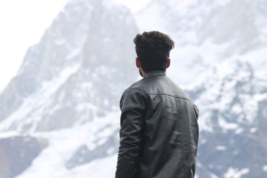 A man in a leather jacket gazes at majestic snow-covered mountains in Haridwar, India.
