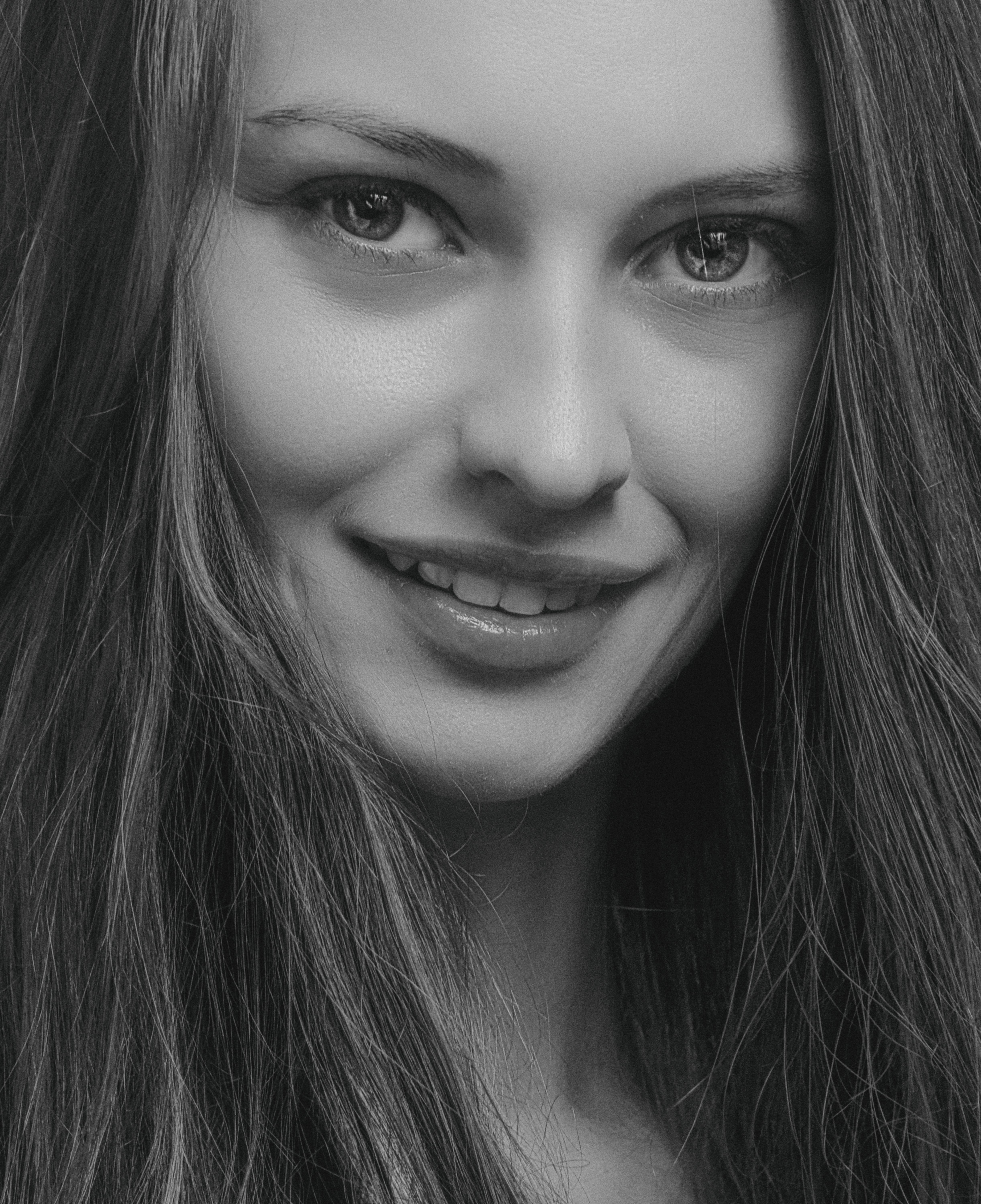 Striking black and white close-up portrait of a smiling woman with long hair.