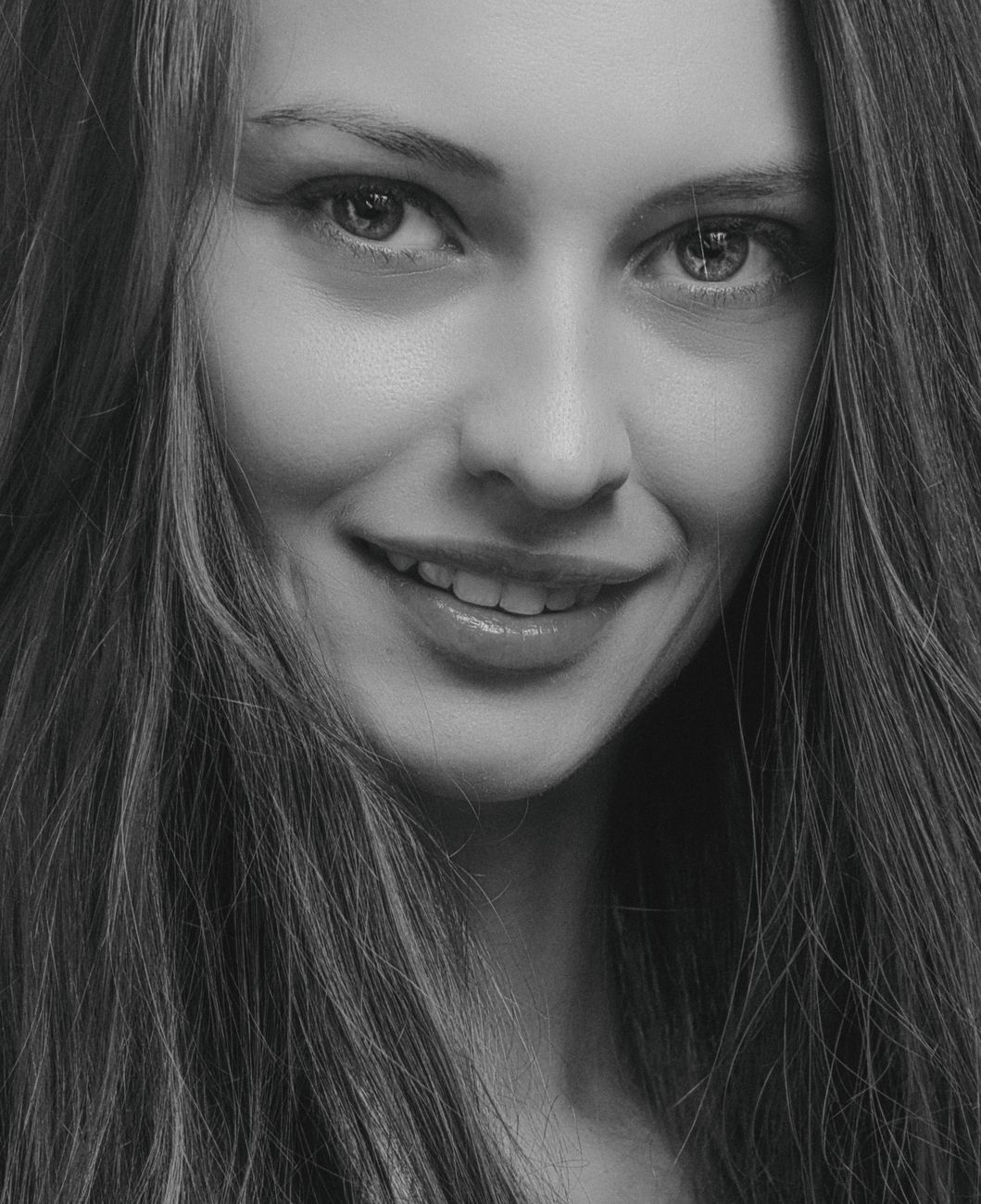 Striking black and white close-up portrait of a smiling woman with long hair.