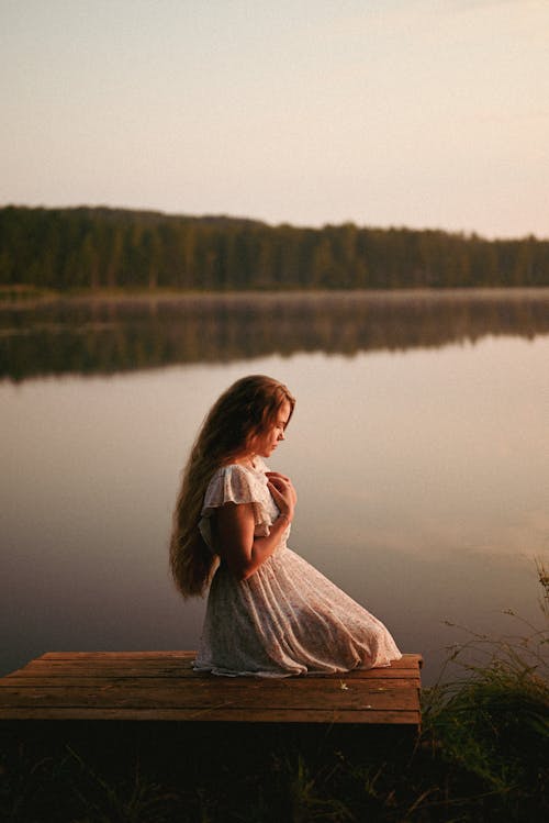 Woman in Long Dress Sitting on Bench by Lake