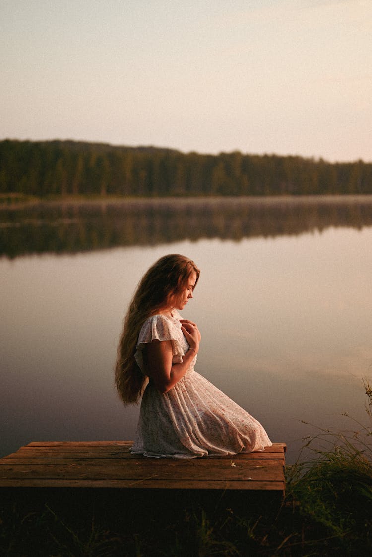 Woman In Long Dress Sitting On Bench By Lake