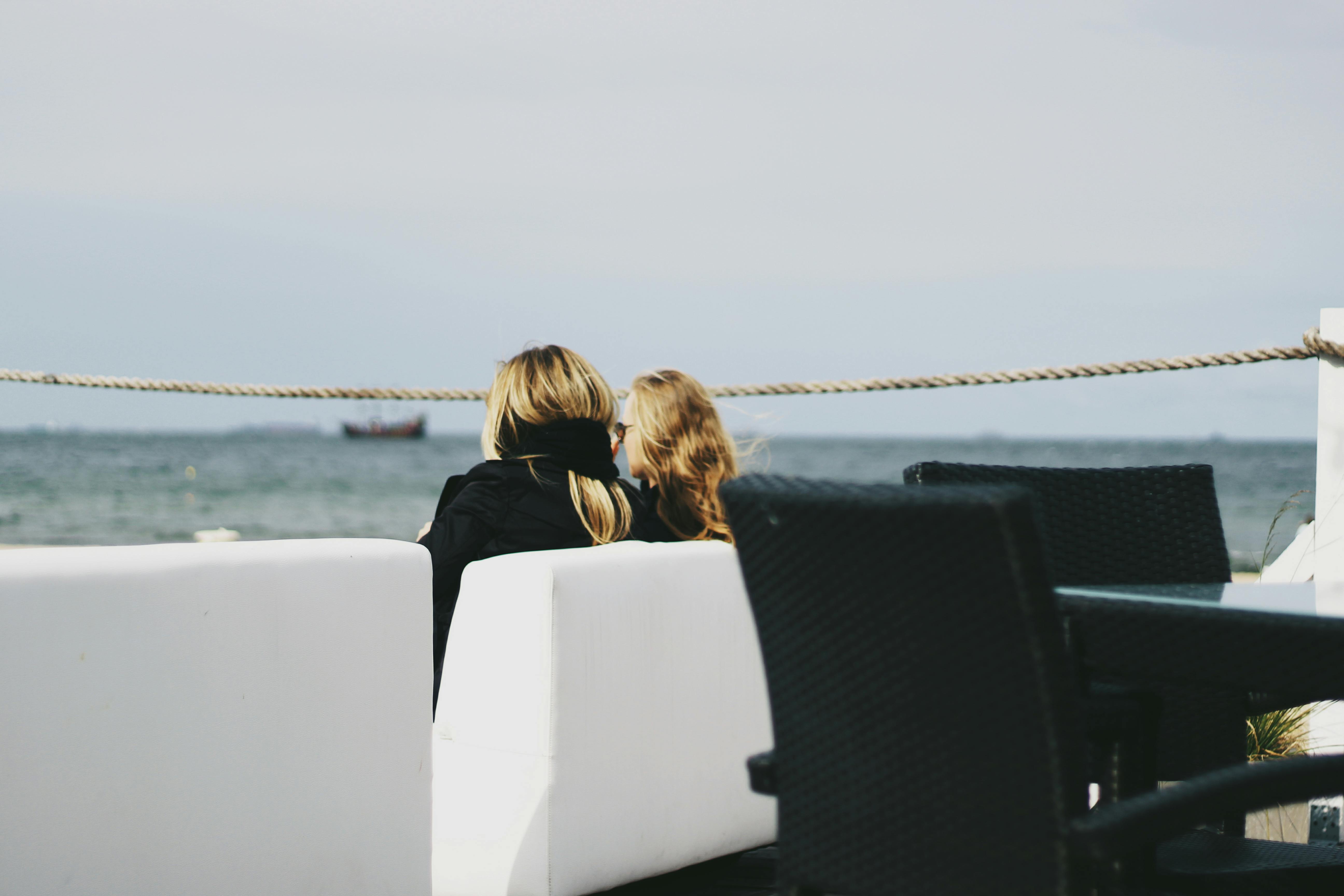 Two women relax on a seaside deck with views of the horizon and watercraft.