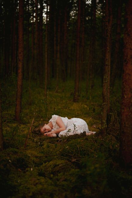A woman in a white dress peacefully sleeping on lush green grass in a dense forest.
