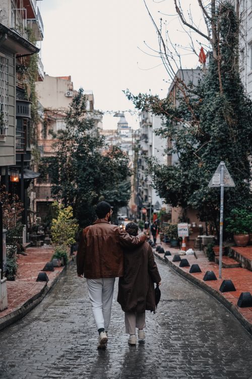 Free Romantic couple walking on a cobblestone street lined with trees, creating a serene urban scene. Stock Photo