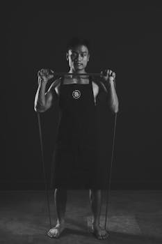 Black and white image of a shirtless man using fitness equipment in a gym setting.