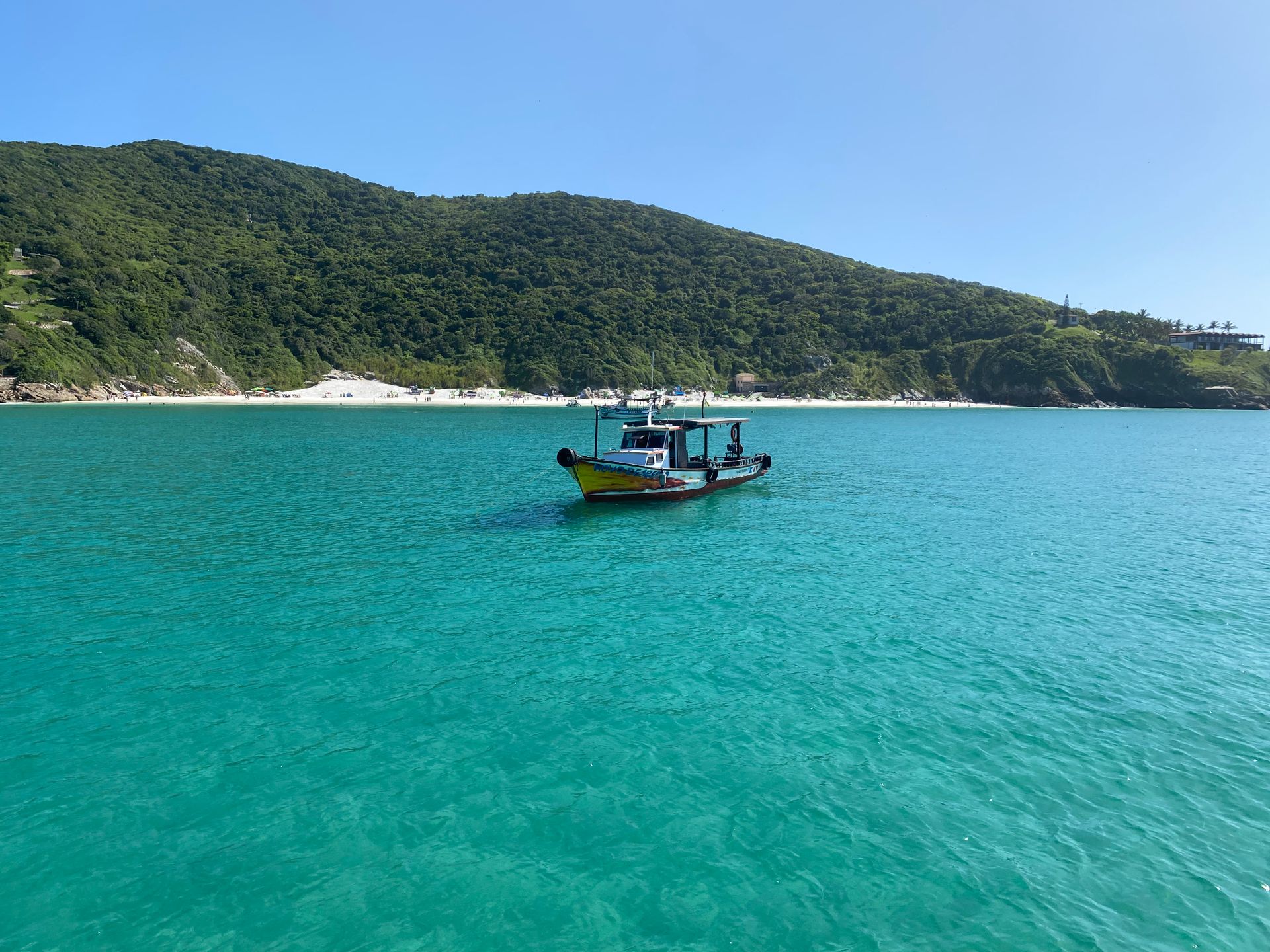 A tranquil scene of a boat floating on clear turquoise waters with lush green hills in the background.