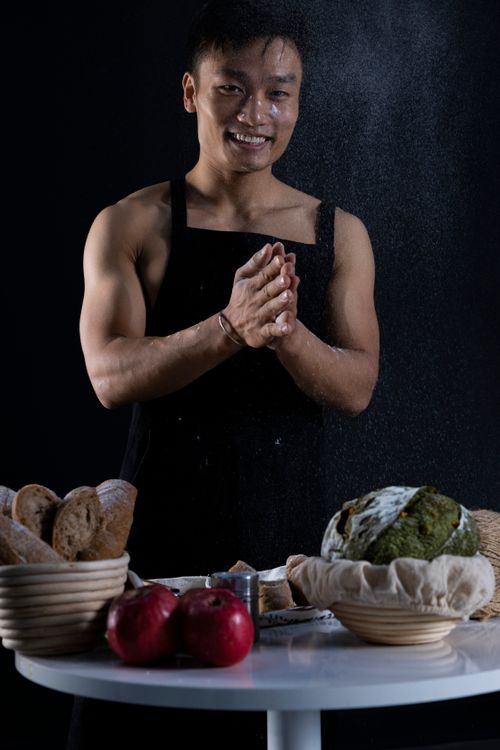 Free Energetic chef in apron smiling while preparing bread on a table with various ingredients. Stock Photo