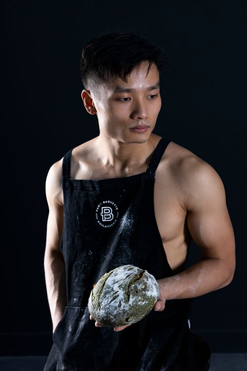 Free A topless Asian male chef in an apron holding freshly baked bread against a dark background. Stock Photo