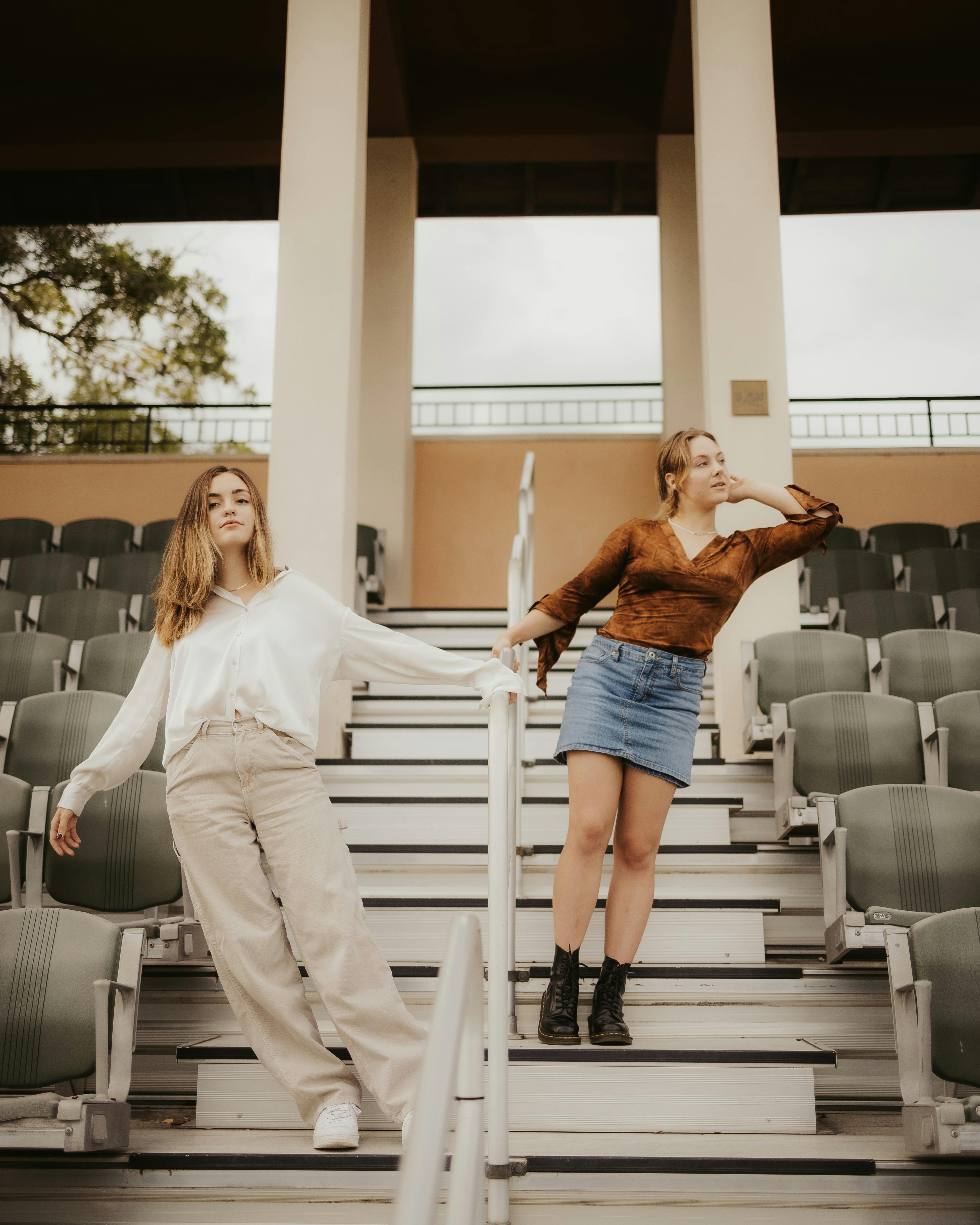 Two fashionable women pose on outdoor bleachers, showcasing modern casual attire and relaxed vibes.