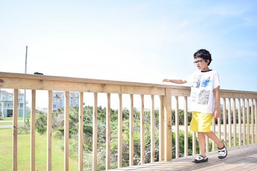 A young boy in casual summer attire enjoys a sunny day outdoors on a wooden deck.