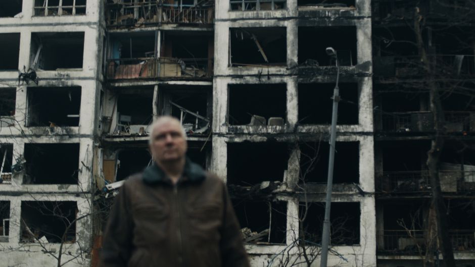 A damaged building in Kyiv, Ukraine with a blurred man in the foreground.