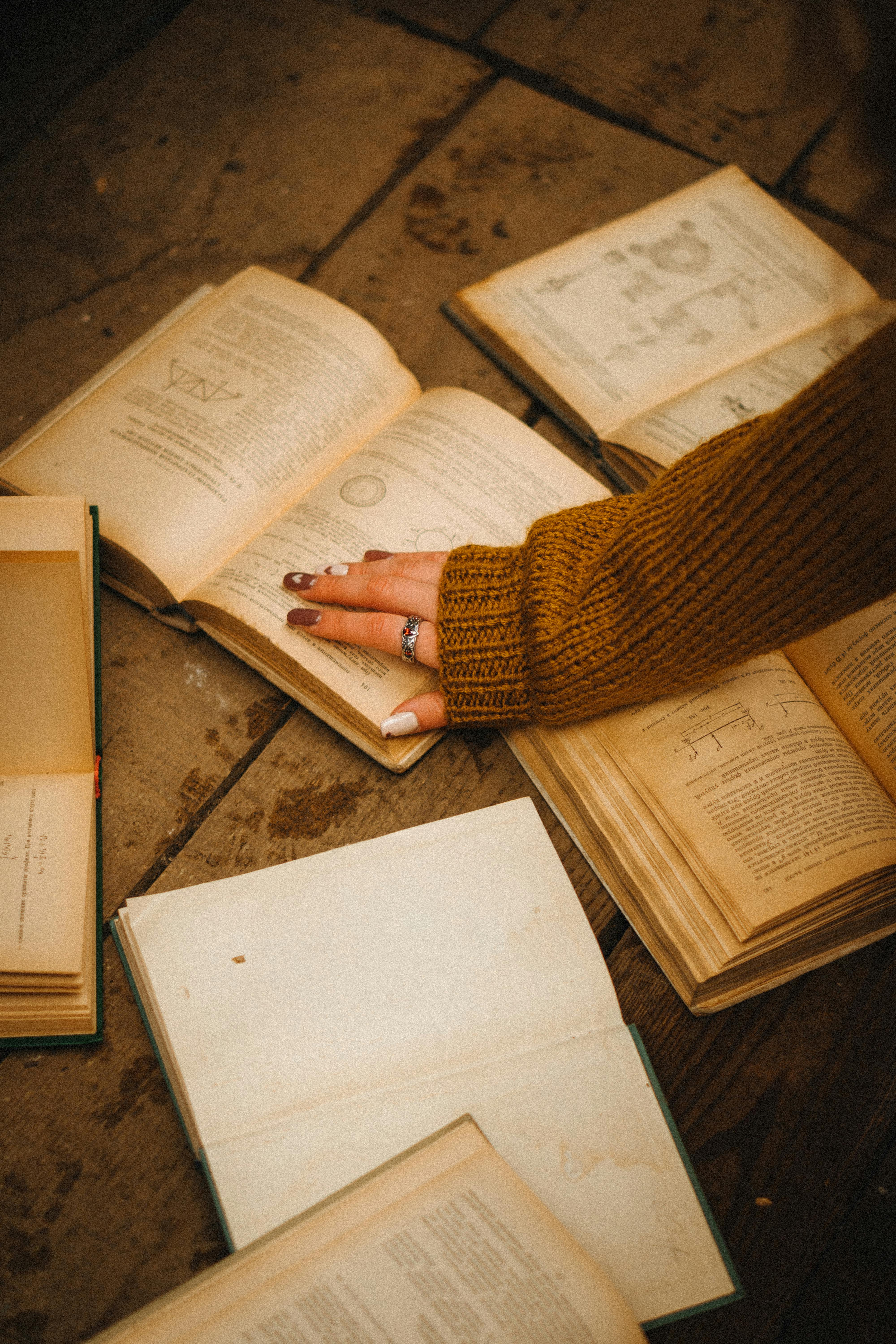 A warm-toned photo of open vintage books with a hand in knitwear, creating a cozy literary vibe.