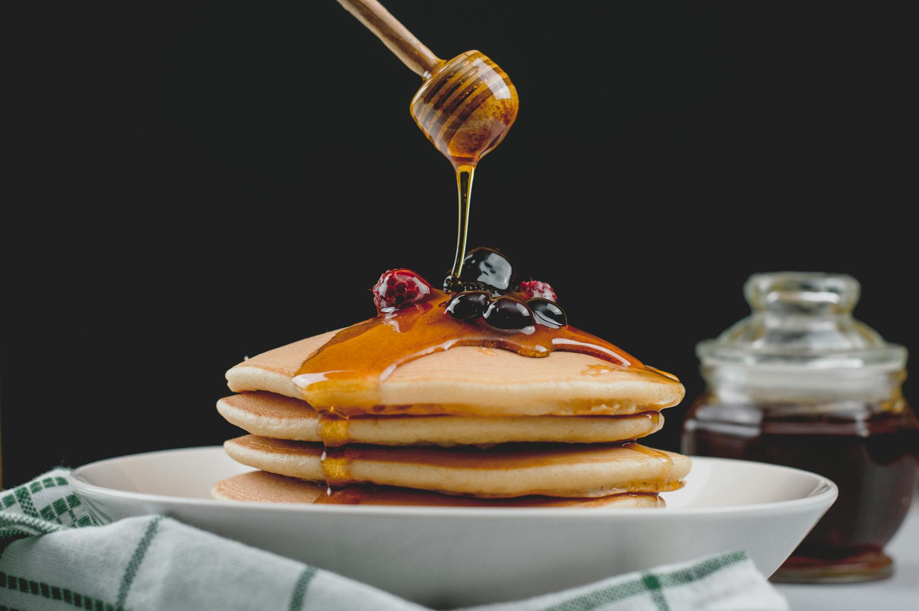 Yacon Syrup In A Glass Jar With A Spoon, Drizzled Over Pancakes Or Desserts, With Yacon Roots In The Background