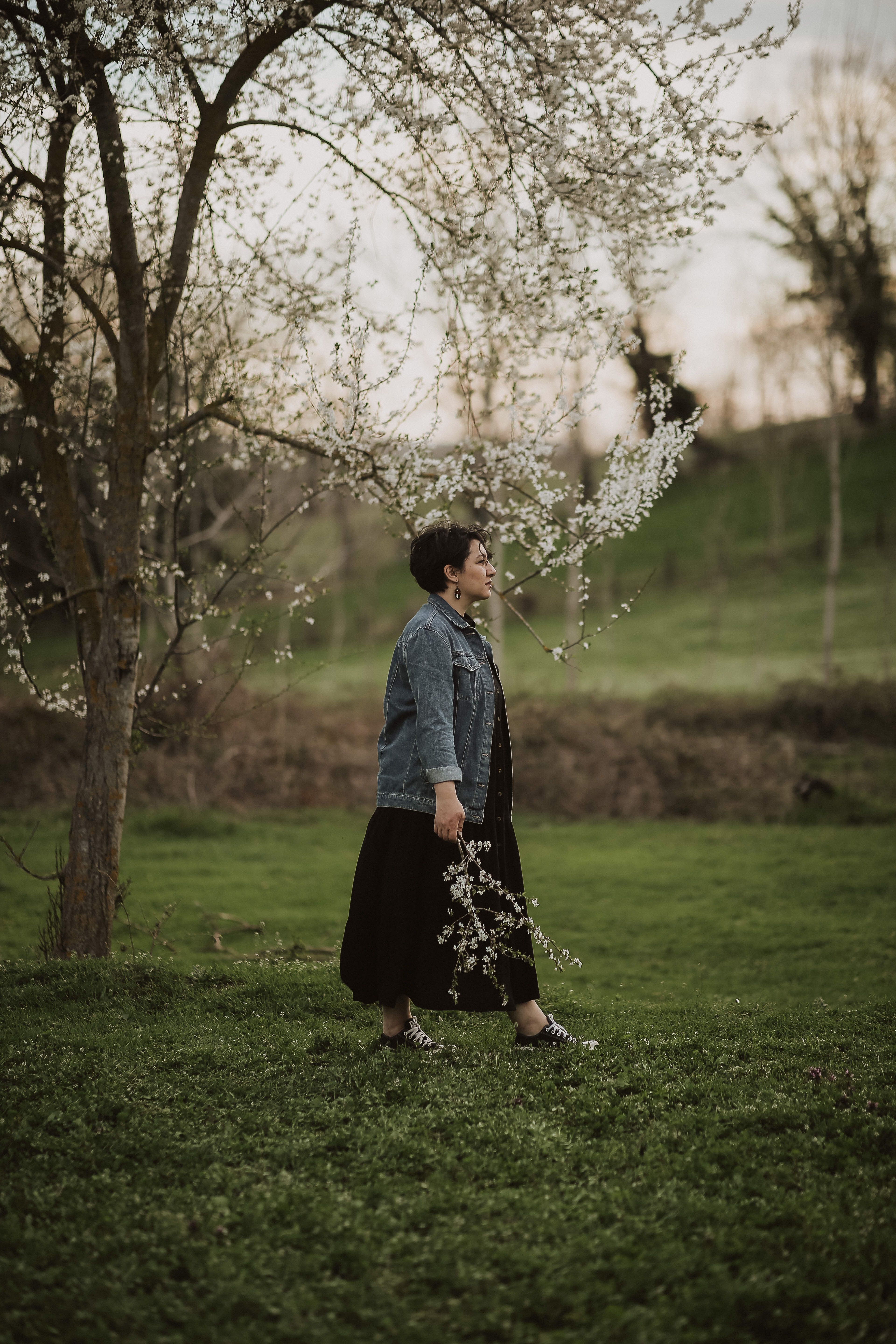 Serene scene of a woman walking through blooming trees in a spring landscape.