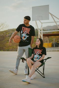 A young couple in matching t-shirts poses on an outdoor basketball court.