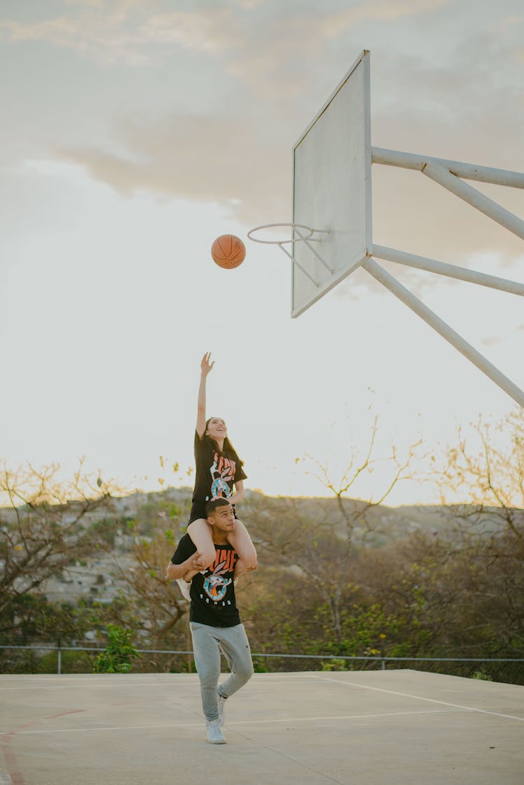 Woman Piggybacking On Mans Shoulder Throwing Basketball