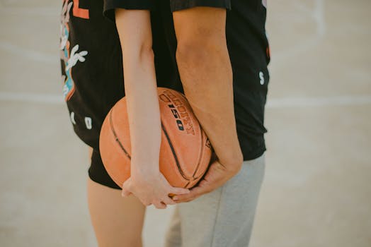 Close-up of two adults holding a basketball together on an outdoor court, symbolizing teamwork and togetherness.