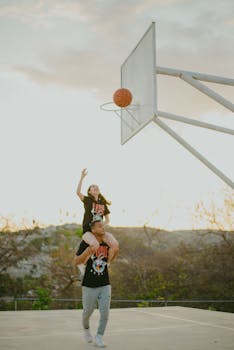 A couple enjoys a fun game of basketball on an outdoor court at sunset, capturing joyful moments together.