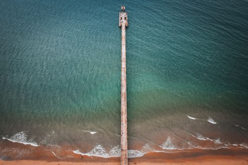 Free Stunning aerial shot of a long pier extending into the vast ocean over sandy shores. Stock Photo