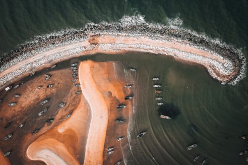 Free A striking top-down view of a rocky peninsula with boats docked along the sandy shore. Stock Photo