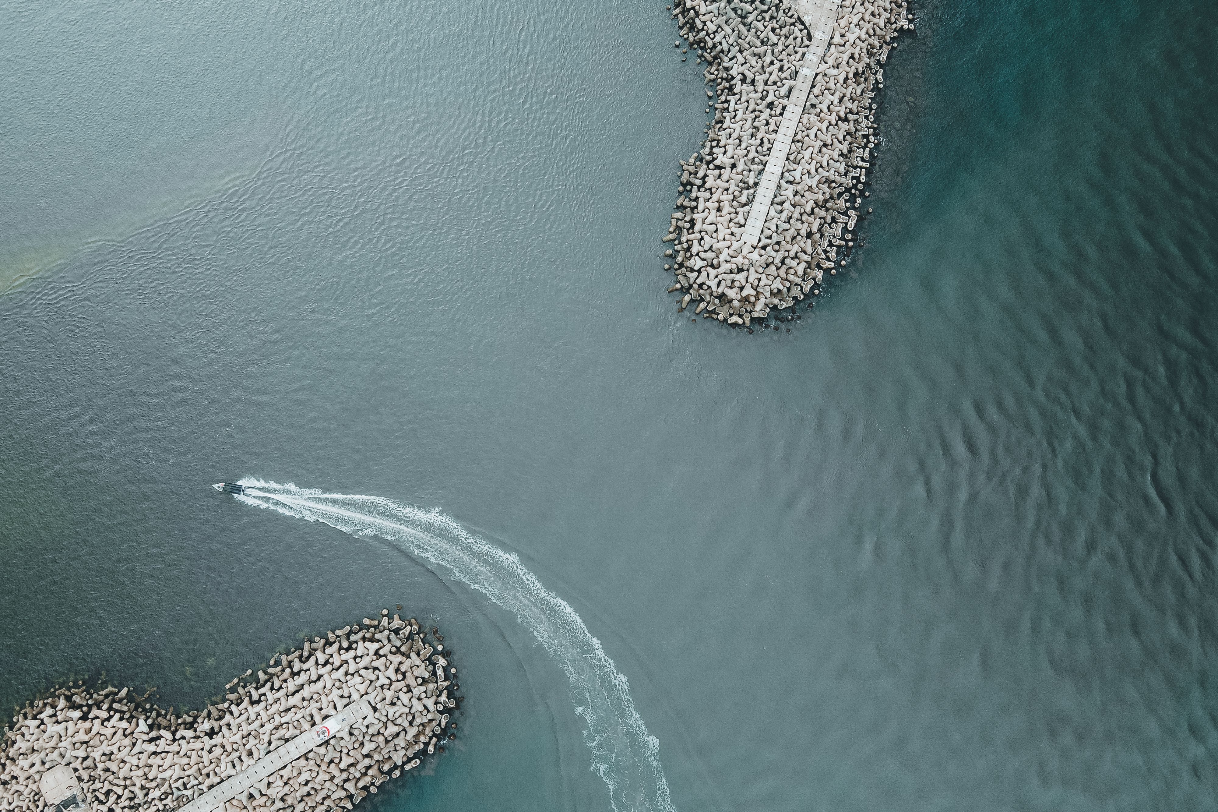 Aerial shot of a motorboat making a turn near rocky breakwaters on the ocean coast.