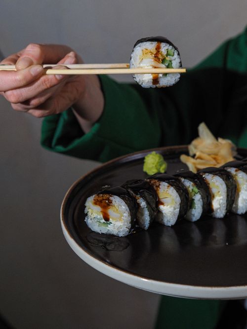 Free A hand holding sushi with chopsticks over a black plate garnished with wasabi and ginger. Stock Photo
