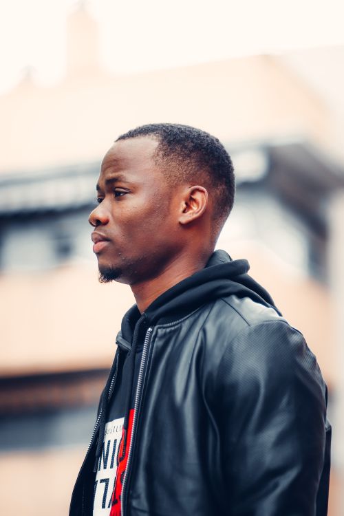 Free A stylish man in a hoodie and leather jacket with an urban background. Perfect for lifestyle and fashion content. Stock Photo