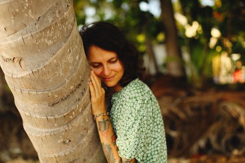 Free A woman with tattoos lovingly leans against a tree in a lush tropical setting, exuding tranquility. Stock Photo