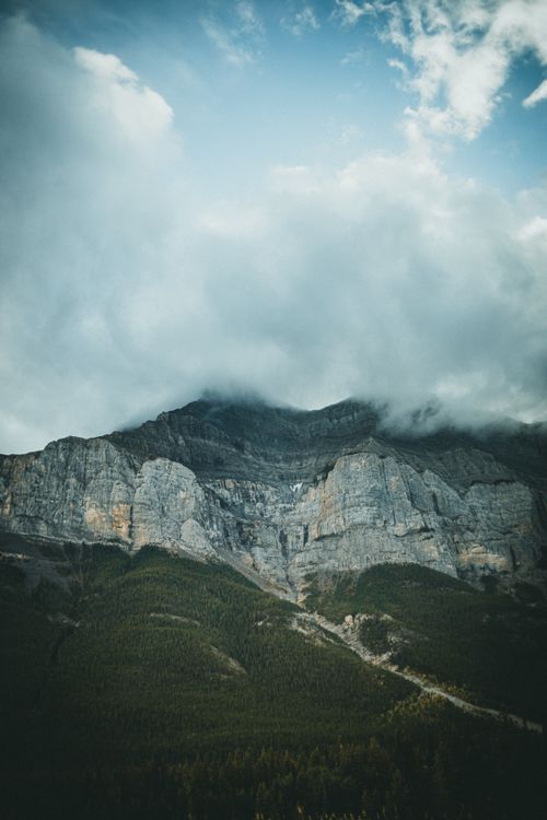 Free A majestic mountain range covered by clouds, with dense forest at its base, perfect for nature lovers. Stock Photo