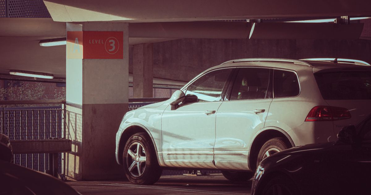 SUV branco estacionado em um estacionamento de vários andares no nível 3 com a luz do sol criando sombras modernas.