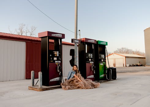 Woman in a ball gown and denim jacket posing at a rural gas station in Des Moines, Iowa.