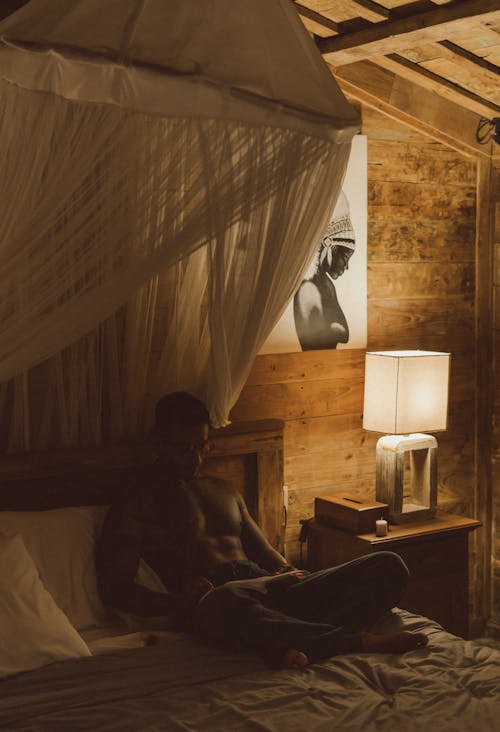 Topless Man Sitting on Bed Reading Book