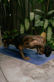 Tattooed young man performs push-ups indoors on a mat, emphasizing fitness and strength.