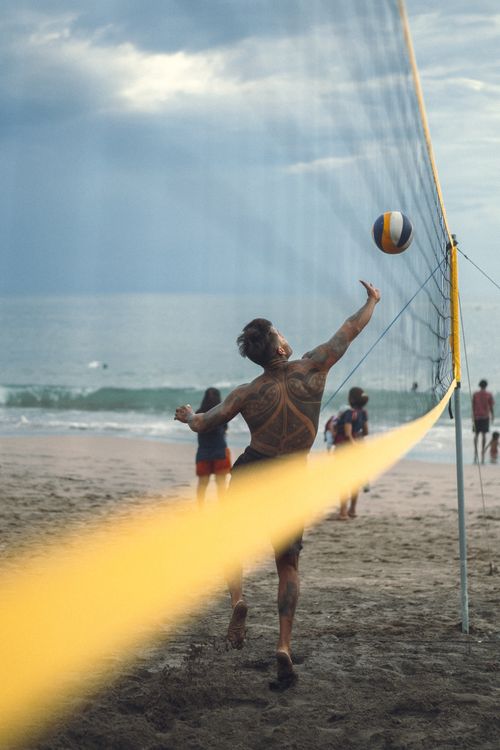 Free A tattooed man playing beach volleyball at the shore, capturing the essence of summer sports. Stock Photo