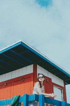 Stylish woman in sunglasses posing by a colorful lifeguard stand on a sunny day.