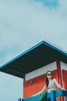 Woman in sunglasses poses at colorful beach tower on a sunny day.