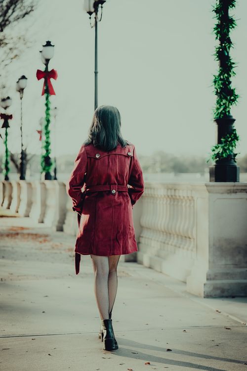 Free Woman in red coat walking on a decorated street, a blend of winter charm and festive atmosphere. Stock Photo
