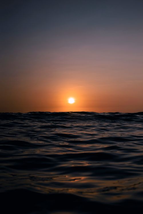 Free Peaceful ocean waves with a vibrant sunset illuminating the sky in warm hues. Stock Photo