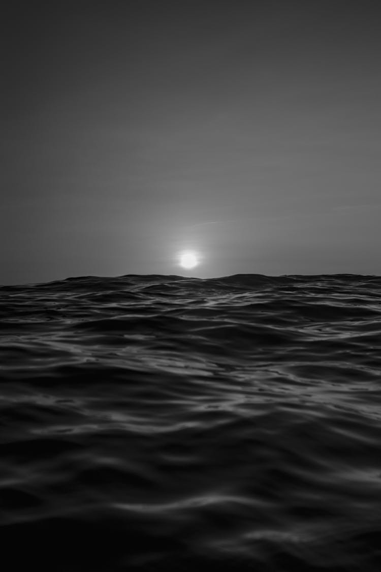 Grayscale Photo Of Ocean Waves With View Of Moon