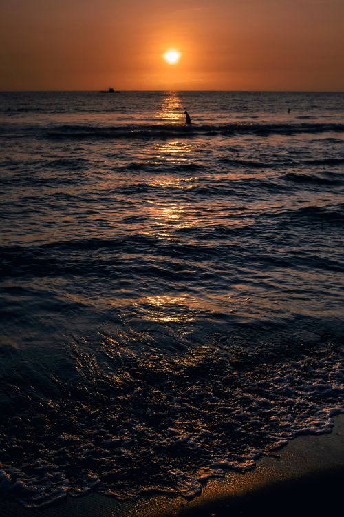 Free Sunset over a calm ocean with a lone surfer creating a serene silhouette on the horizon. Stock Photo
