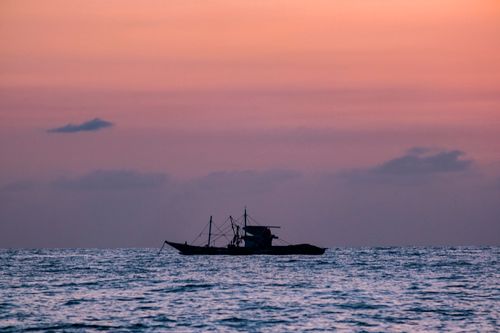 Free A serene silhouette of a fishing boat at sea during a picturesque sunset, capturing peaceful nautical beauty. Stock Photo
