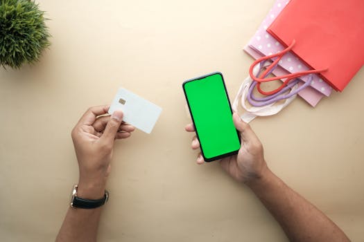 Top view of hands holding a smartphone and credit card for online shopping on a beige background.