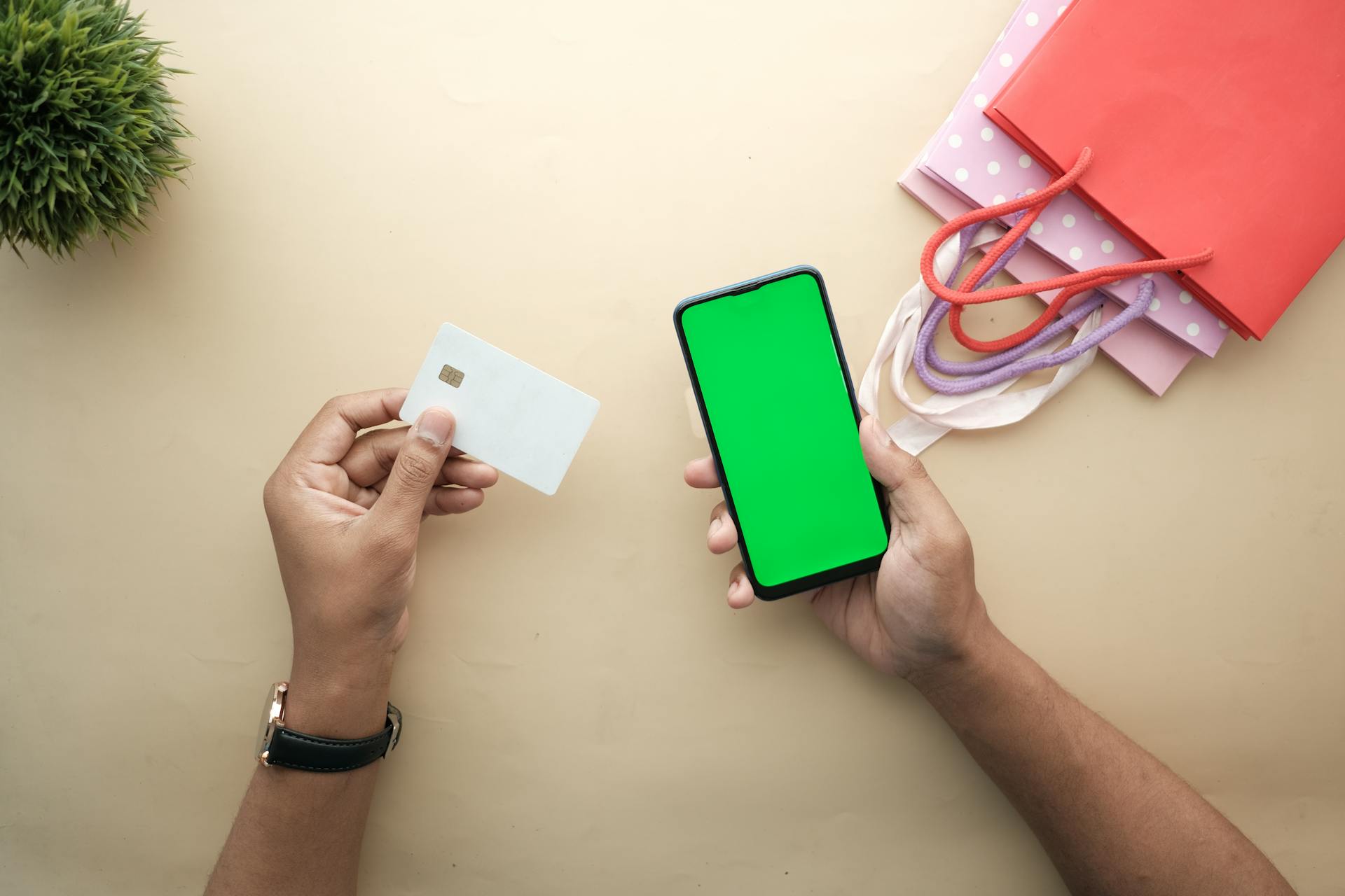 Top view of hands holding a smartphone and credit card for online shopping on a beige background.