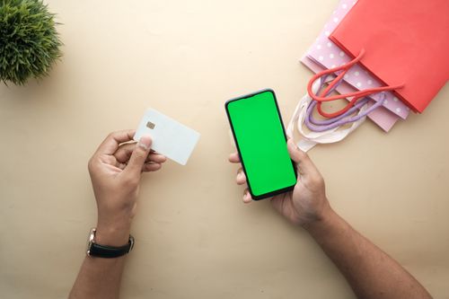 Free Top view of hands holding a smartphone and credit card for online shopping on a beige background. Stock Photo