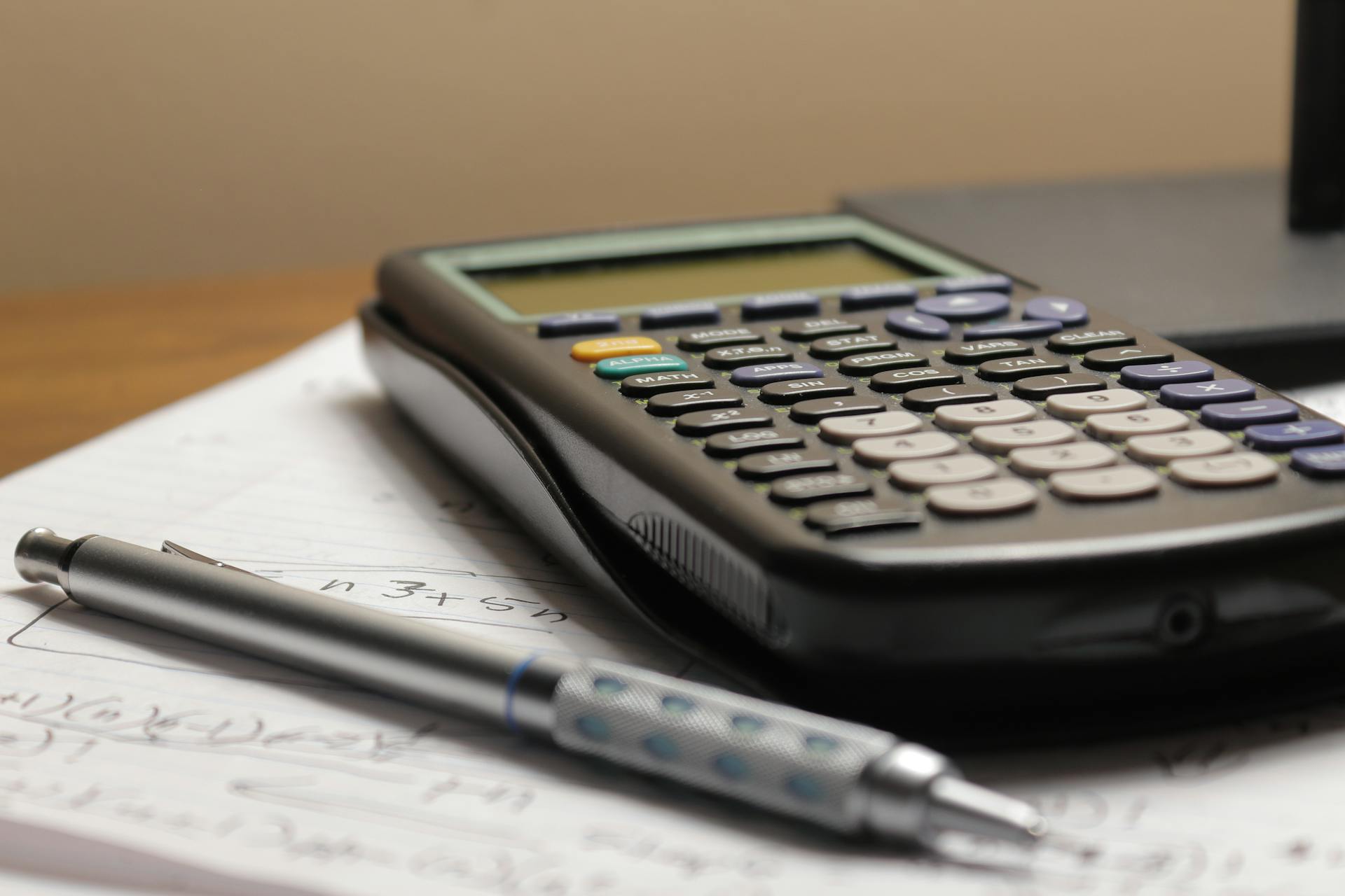 A detailed view of a calculator and pen resting on mathematical notes, ideal for educational and financial themes.