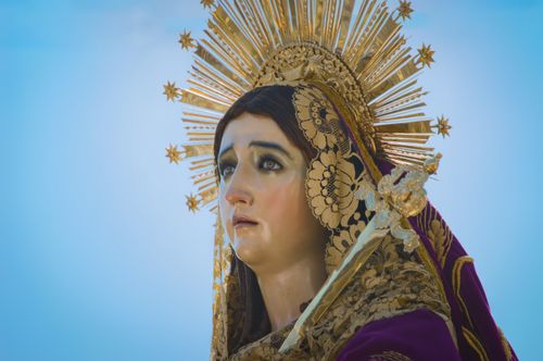 Free Close-up of a Virgin Mary statue with a golden crown against a clear blue sky. Stock Photo