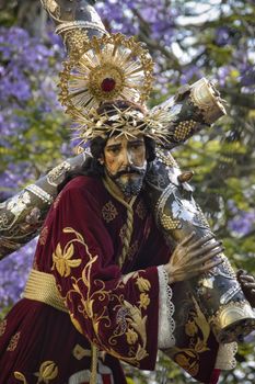 Statue of Jesus Christ carrying the cross with intricate garments and crown in a natural setting.