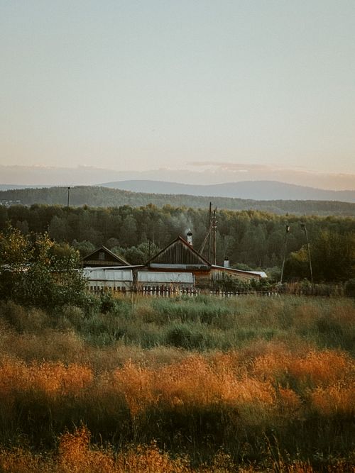 Free Charming rural farmhouse amidst fields and forest at sunset. Stock Photo