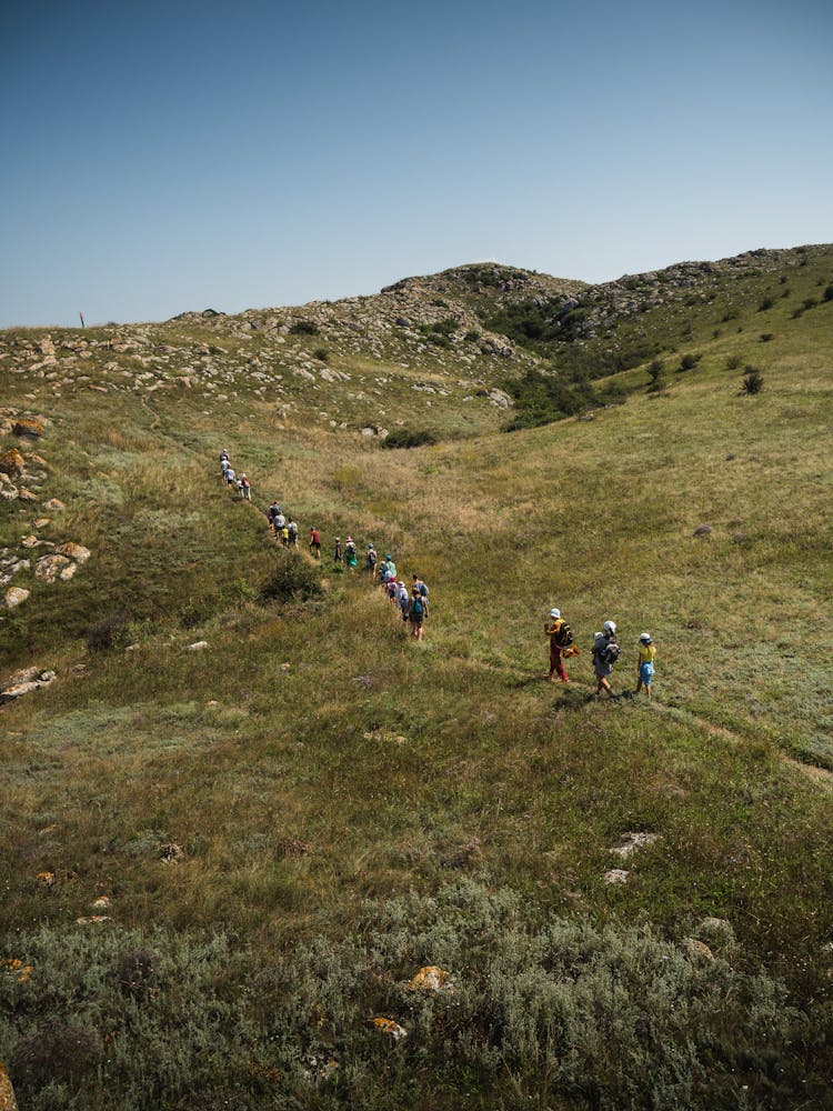 People Climbing Grassy Slope Of Mountain