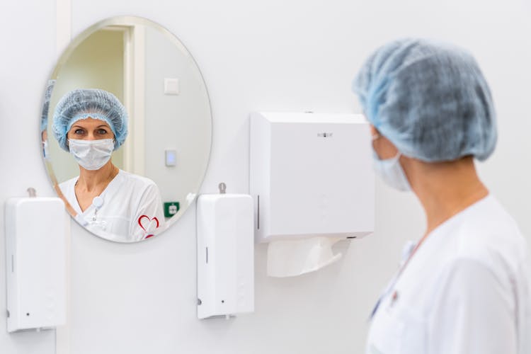 Doctor In Scrub Hat Staring At Her Reflection In Mirror